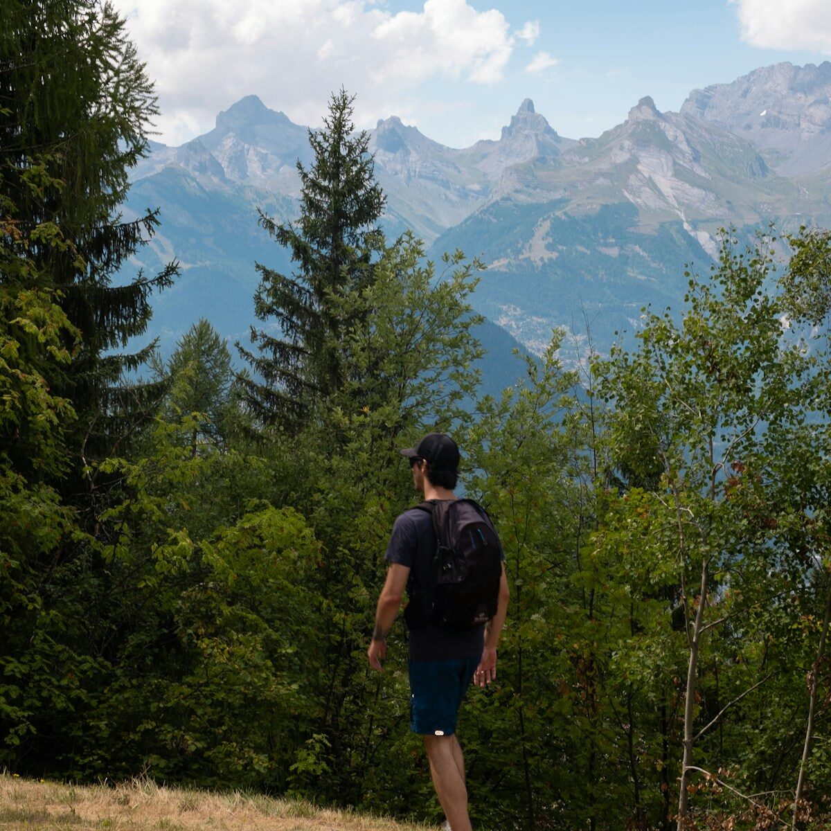 Photo by Geoffrey Chevtchenko a man walking on a trail in front of trees and mountains