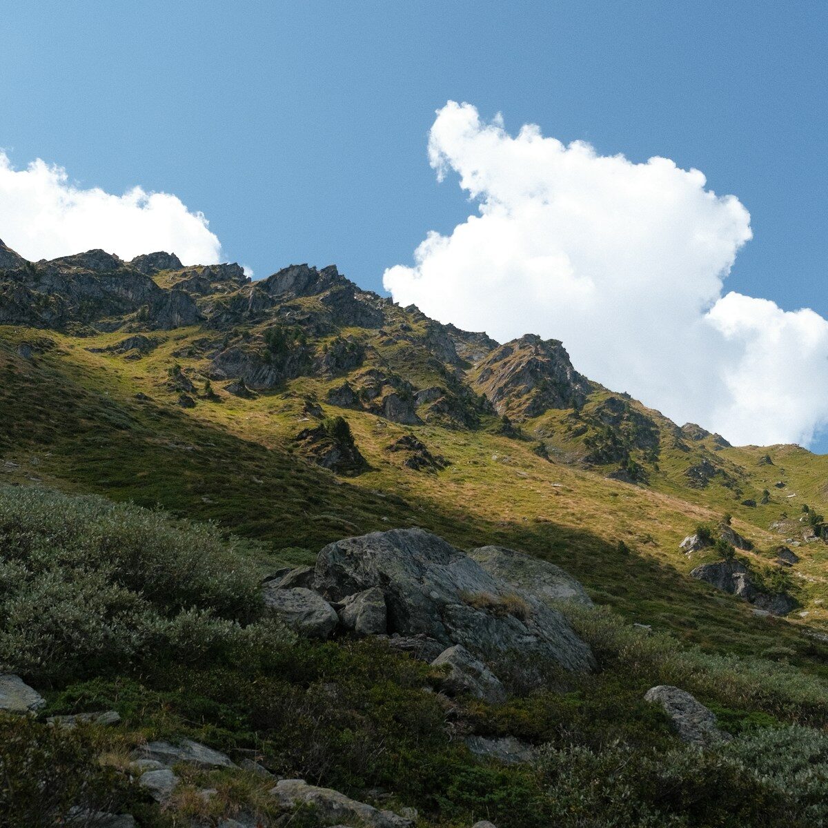 Photo by Geoffrey Chevtchenko a grassy hill with rocks and a cloudy sky